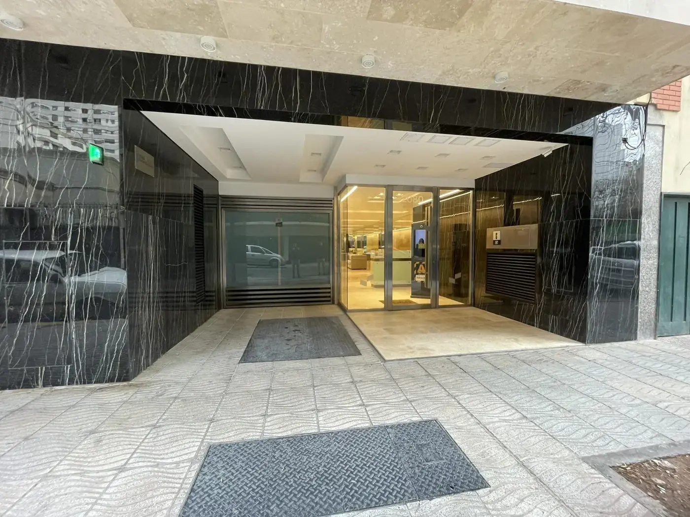 Ingreso de edificio con piso de piedra, mármol negro veteado y puertas de vidrio